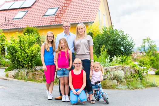 Young family with Mother, father and daughters standing in front of home in housing estate