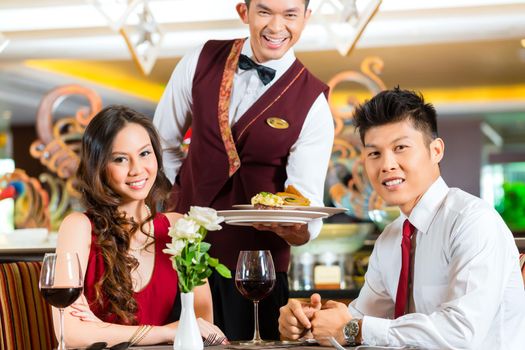 Asian Chinese couple - Man and woman - or lovers having a date or romantic dinner in a fancy restaurant while the waiter is serving food