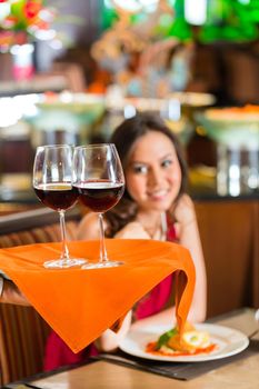 Waiter or steward serving woman or couple red wine in glasses on a tray in a fancy restaurant or hotel