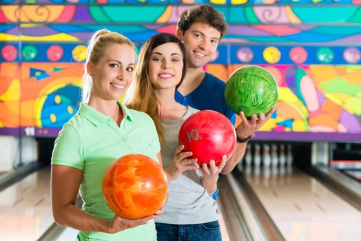 Young people or friends, man and women, playing bowling with a ball in front of the ten pin alley, they are a team