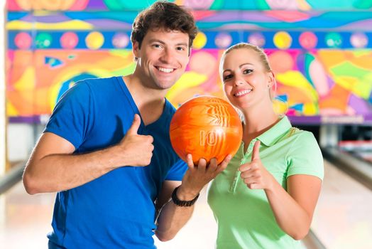 Young couple or friends, man and woman, playing bowling with a ball in front of the ten pin alley, they are a team