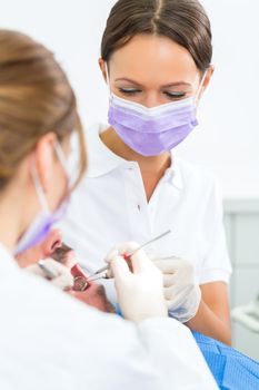 dentist in her practice or office treating male patient with assistant wearing masks and gloves