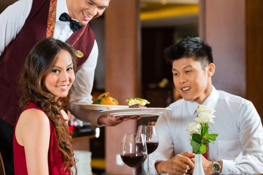 Asian Chinese couple - Man and woman - or lovers having a date or romantic dinner in a fancy restaurant while the waiter is serving food