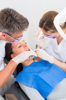 Female patient with dentist and assistant in a dental treatment, wearing masks and gloves