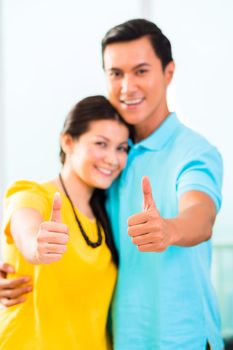 Young Asian handsome couple in apartment with city view showing thumbs up