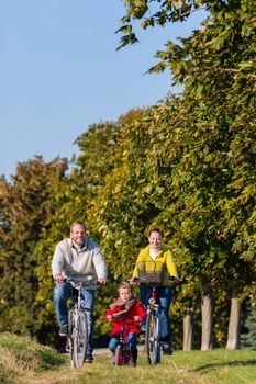 Family with mother, father and daughter having family trip on bicycle or cycle in park
