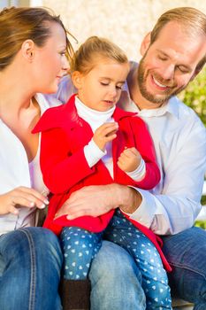 Family with mother, father and daughter together on garden bench in front of home