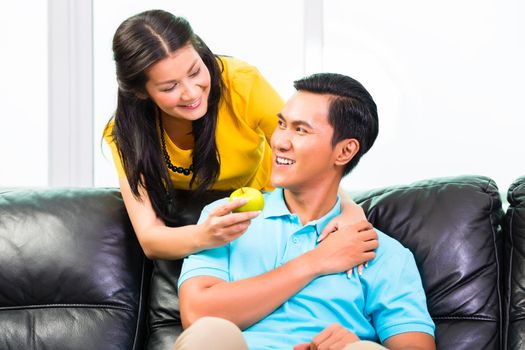 Young Asian Couple handsome woman romantic feeding boyfriend with apple on sofa or couch