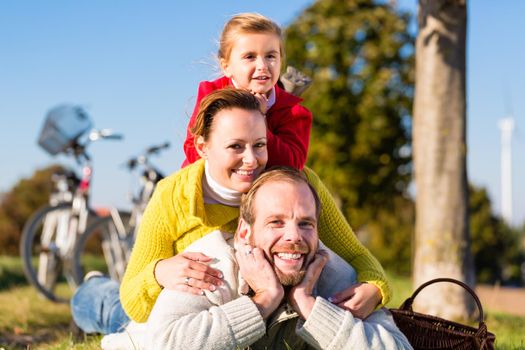 Family with mother, father and daughter having break on family trip with bicycle or cycle in park