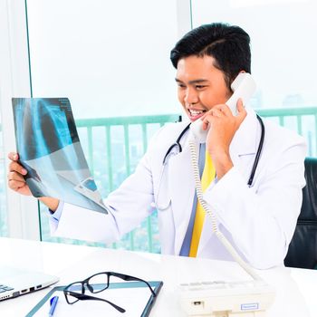 Asian doctor telephoning about diagnosis X-ray photograph in his medical office