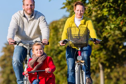 Family with mother, father and daughter having family trip on bicycle or cycle in park