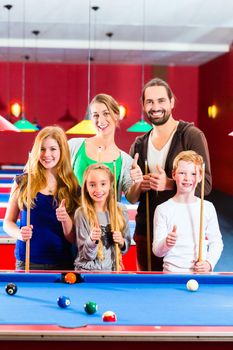 Family playing together billiard with queue and balls on pool table