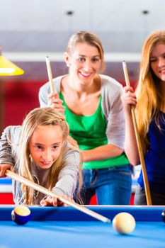 Family playing together billiard. Brother kick off with queue and balls on pool table