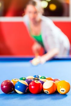 Couple or friends playing billiard with queue and balls on pool table