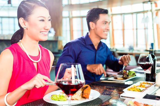 Asian people having dinner and drinking red wine in very fancy restaurant with open kitchen in background