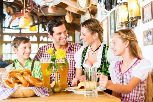 Bavarian girl wearing dirndl and eating with family in traditional restaurant