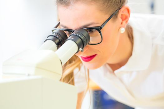 Female dental technician or orthodontist controlling denture with microscope and grinder