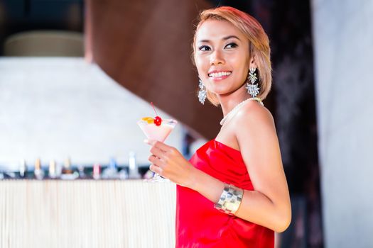 Asian woman drinking cocktails in fancy bar or club