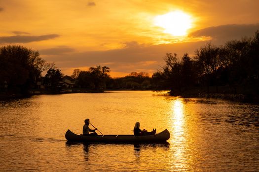 Silhouette of couple with dog kayaking in a lake at sunset, romantic scene