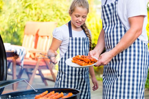 Family of Father and daughter barbecue meat spits at family garden BBQ