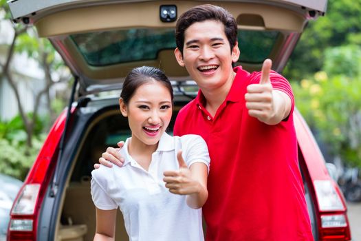 Asian couple loading suitcase for travel in luggage trunk of car