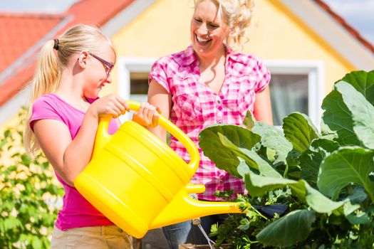 Mother and daughter working in garden watering plants with can in front of their house