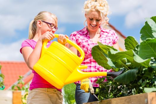 Mother and daughter working in garden watering plants with can in front of their house