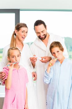 Parents and children cleaning tooth together in bathroom