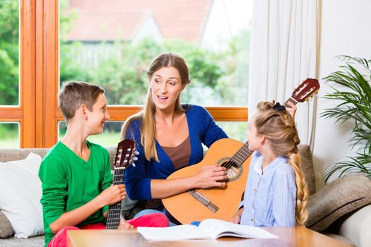 Family making music at home with guitar, mother, daughter and son playing