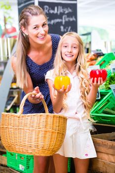 Mother and daughter selecting vegetables while grocery shopping in organic supermarket