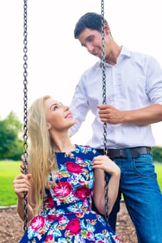 Man and woman on swing in park, couple in love