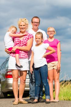 Family of Parents and children standing in front of car in countryside