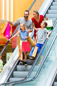 Family in shopping mall on escalators with bags