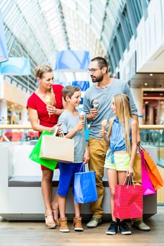 Family eating ice cream in shopping mall with bags