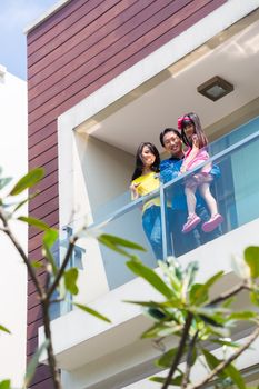 Asian Chinese family of parents and child standing proud on modern home balcony