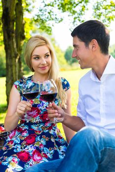 Couple having picnic wit red wine on meadow sitting on blanket with basket