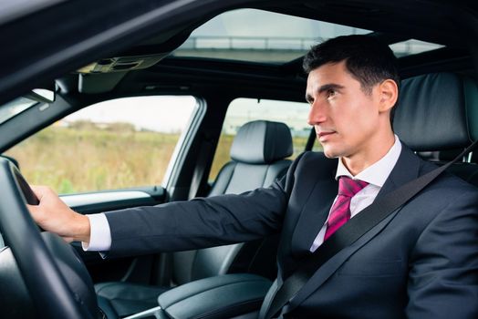 Man driving his car for business travel wearing a suit