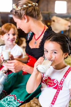 Bavarian mother sitting with children in cowhouse on hay bale drinking fresh milk