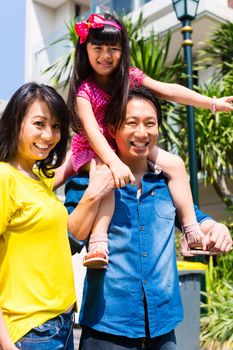 Asian Chinese family of parents and child standing proud in front of modern home