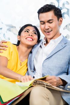 Asian couple buying sofa in furniture store, sitting on couch choosing color and material