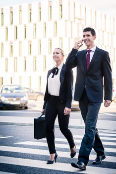 Business people in front of office building wearing briefcase and talking to smart phone