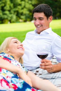 Couple drinking red wine on grass of park at picnic