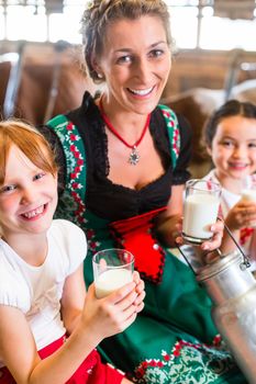 Bavarian mother sitting with children in cowhouse on hay bale drinking fresh milk