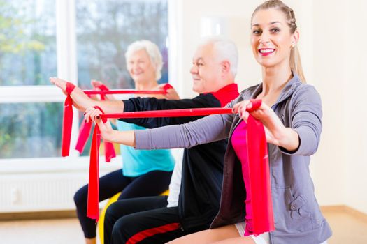 People, young and senior, at gym exercise with stretch band