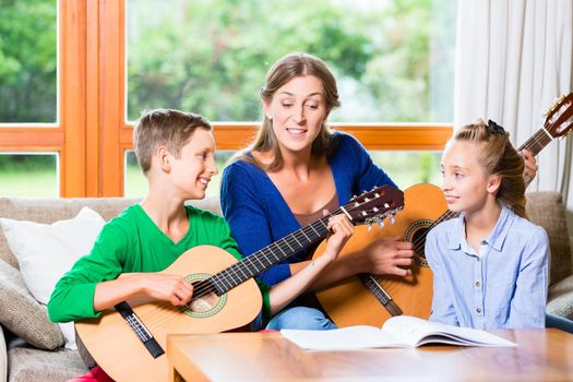 Family making music at home with guitar, mother, daughter and son playing