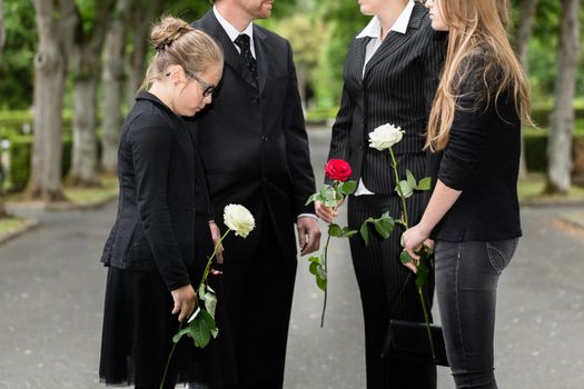 Family mourning on funeral at cemetery standing in group with flowers