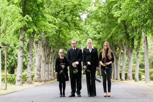 Family on cemetery walking down alley at graveyard with roses