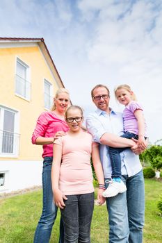 Family standing in front of home or house, mother, father and two children