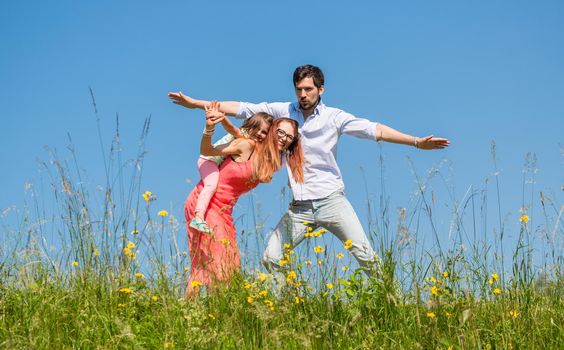 Family doing the plane on summer meadow under clear blue sky