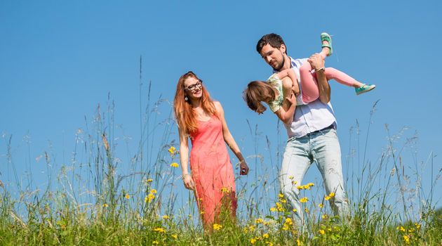 Family doing the plane on summer meadow under clear blue sky